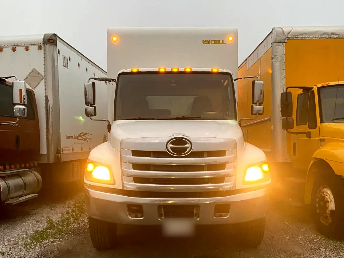 A Bravo 24 Transport Ltd. cube truck in the yard at first light, headlights on, flanked by trailers.